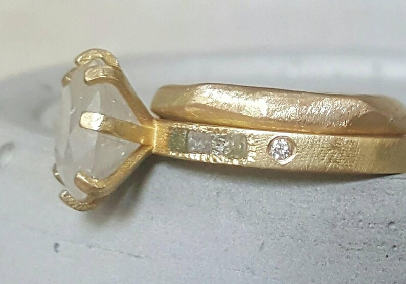 May include: A gold ring with a large, clear gemstone set in a prong setting. The ring is paired with a matching band with a smaller diamond accent.