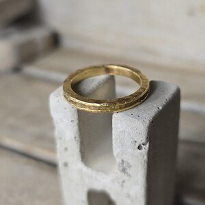 Pu&ograve; includere: Un anello a fascia d'oro con una texture martellata. L'anello &egrave; appoggiato su un blocco di cemento.