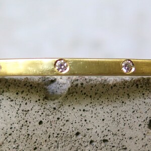 May include: A thin gold bangle bracelet with five small diamonds set into the band.