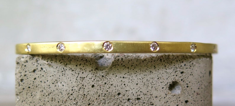 May include: A thin gold bangle bracelet with five small diamonds set into the band.