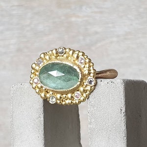 Pode incluir: Um anel de ouro com uma gema verde cercada por diamantes menores e pedras preciosas rosa.