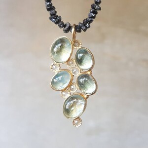 Pu&ograve; includere: Una delicata collana d'oro con un ciondolo che presenta un gruppo di pietre di acquamarina blu chiaro e piccoli diamanti trasparenti. La collana &egrave; realizzata con perline nere.