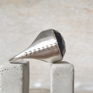May include: A silver ring with a faceted black gemstone. The ring has a textured band.