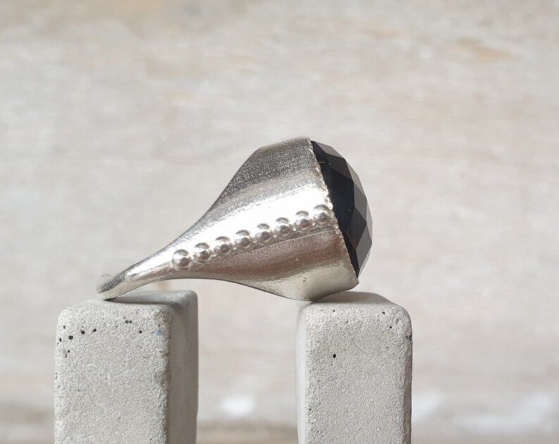 May include: A silver ring with a faceted black gemstone. The ring has a textured band.