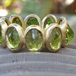 May include: A gold ring with a row of green gemstones. The ring is set with round, faceted stones that are bezel set in the gold.
