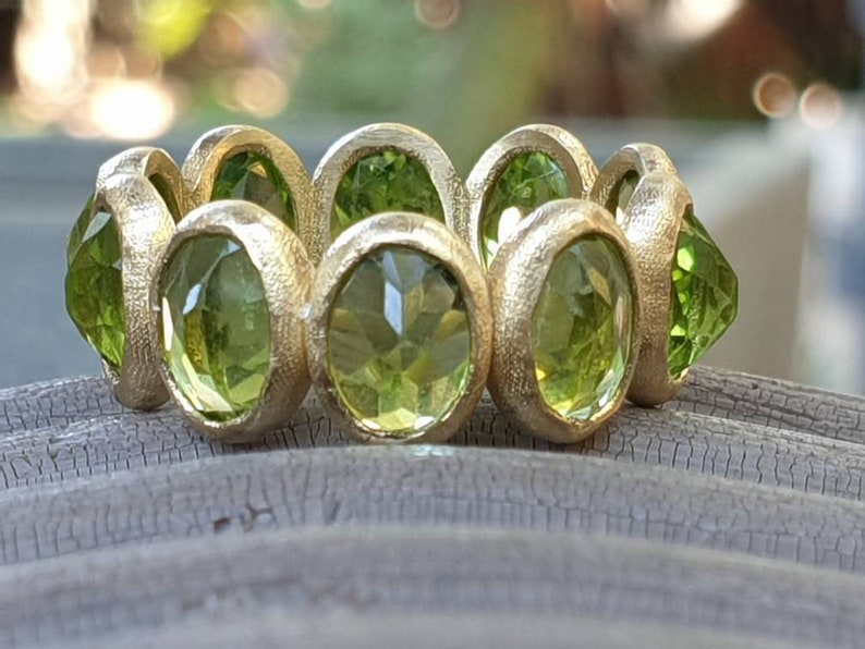 May include: A gold ring with a row of green gemstones. The ring is set with round, faceted stones that are bezel set in the gold.