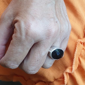 May include: A silver ring with a black gemstone. The ring is on a person's finger.