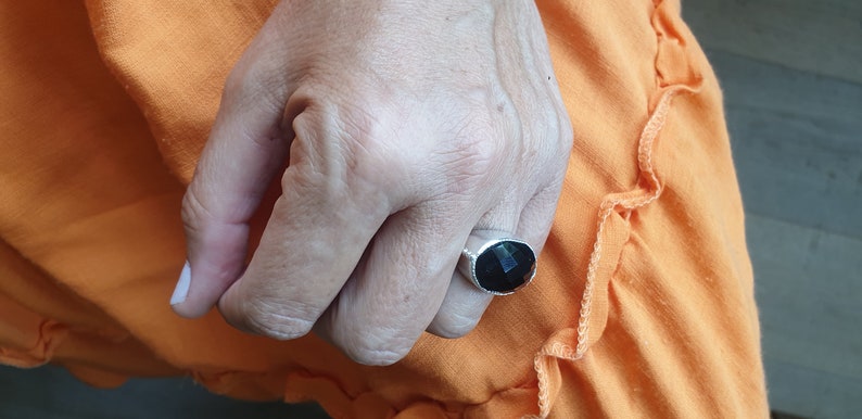 May include: A silver ring with a black gemstone. The ring is on a person's finger.