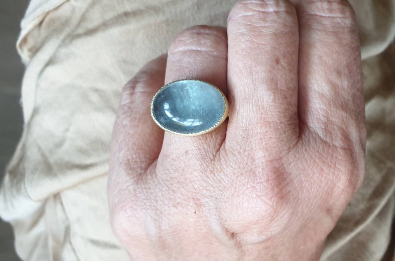 May include: A ring with a large oval-shaped blue gemstone set in a gold band.