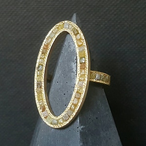 May include: A gold ring with an oval-shaped setting. The setting is filled with small, colorful diamonds.