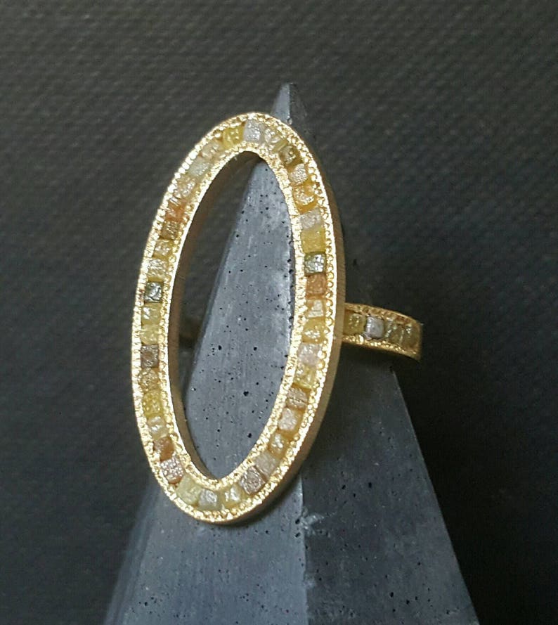May include: A gold ring with an oval-shaped setting. The setting is filled with small, colorful diamonds.