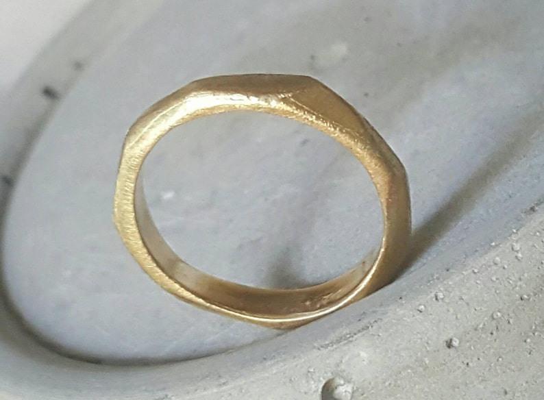 May include: A gold ring with a textured, irregular shape. The ring is thick and has a rounded edge.