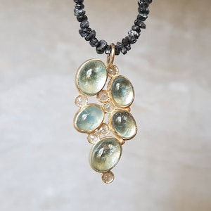 Pu&ograve; includere: Una collana con un ciondolo in oro decorato con un gruppo di pietre di acquamarina blu chiaro e piccoli diamanti bianchi. La collana &egrave; realizzata con perle di diamanti neri.