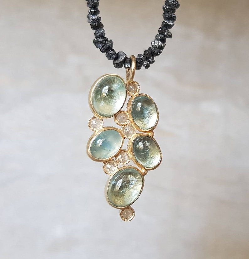 Pu&ograve; includere: Una collana con un ciondolo in oro decorato con un gruppo di pietre di acquamarina blu chiaro e piccoli diamanti bianchi. La collana &egrave; realizzata con perle di diamanti neri.