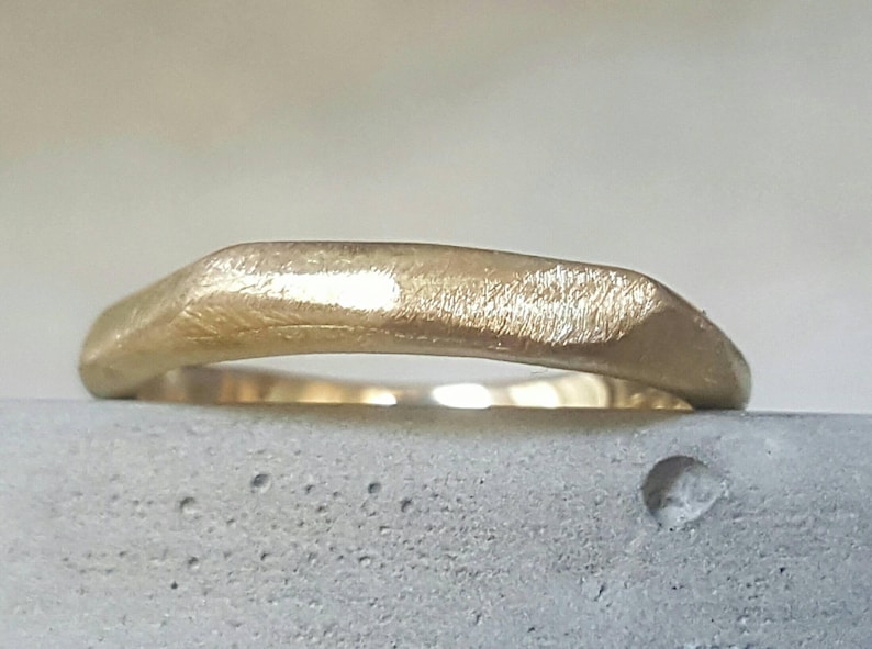 May include: A gold band ring with a textured, hammered finish. The ring is slightly curved and has a rounded edge.