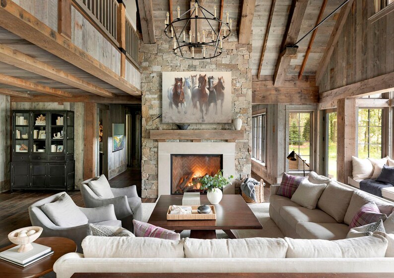 May include: A large living room with a stone fireplace and a painting of horses above it. The room has a vaulted ceiling with exposed wooden beams and large windows. There are several couches and chairs arranged around a coffee table.
