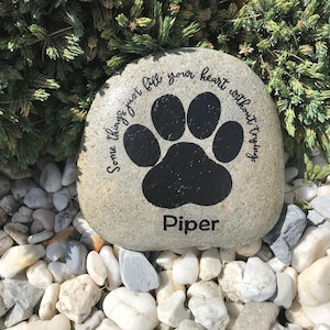 Pode incluir: Uma pedra cinza com uma pegada de pata preta e o texto "Some things just fill your heart without trying." e "Piper" pintado nela.