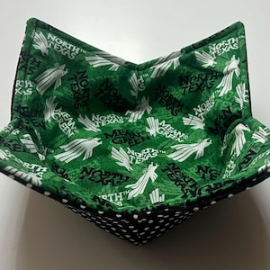 May include: A green and black fabric bowl with a white and green pattern. The pattern features the words "North Texas" and "Mean Green".