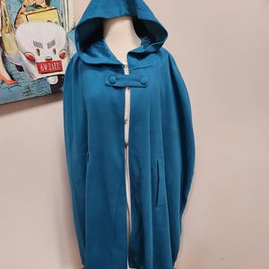 May include: Teal hooded cape with a button closure and a pocket on the side.