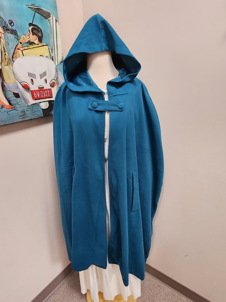 May include: Teal hooded cape with a button closure and a pocket on the side.