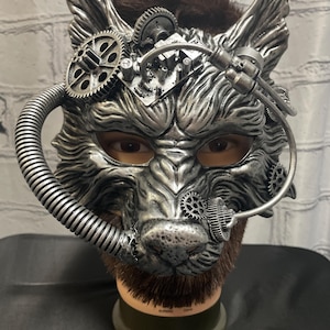 May include: A silver wolf mask with steampunk details, including gears, pipes, and a faux fur beard. The mask is on a mannequin head.