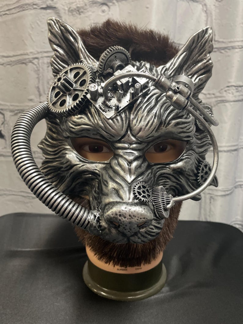 May include: A silver wolf mask with steampunk details, including gears, pipes, and a faux fur beard. The mask is on a mannequin head.