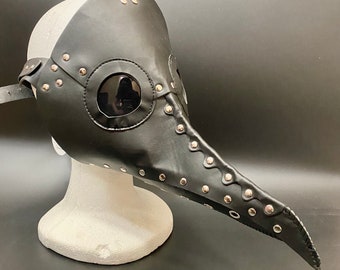 May include: A black leather plague doctor mask with a long beak and silver studs. The mask has a clear plastic eye piece.