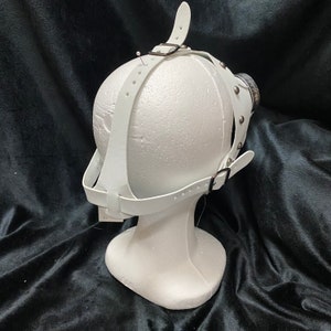 Peut inclure: Masque en cuir blanc avec des sangles r&eacute;glables et des clous argent&eacute;s. Le masque est sur une t&ecirc;te de mannequin blanche.