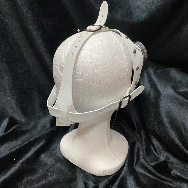 Peut inclure: Masque en cuir blanc avec des sangles r&eacute;glables et des clous argent&eacute;s. Le masque est sur une t&ecirc;te de mannequin blanche.