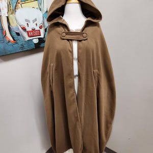 May include: A brown hooded cape with two buttons on the front. The cape is made of a soft, warm fabric and has a relaxed fit.