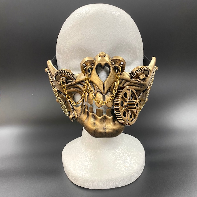 Peut inclure: Un masque de style steampunk dor&eacute; avec des engrenages et des cha&icirc;nes complexes. Le masque est fix&eacute; &agrave; une t&ecirc;te de mannequin blanche.