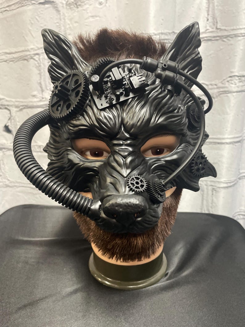 May include: A black wolf mask with steampunk details, including gears, pipes, and a circuit board. The mask is on a mannequin head with brown hair.