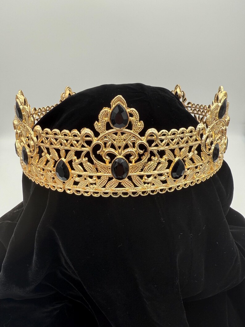 May include: A gold-colored crown with intricate filigree and black gemstone accents. The crown features a series of teardrop-shaped gems and floral designs. The crown is designed for special occasions and events.