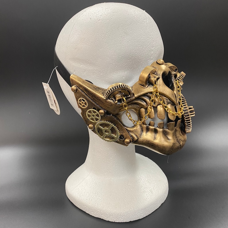Peut inclure: Un masque de style steampunk dor&eacute; avec des engrenages et une cha&icirc;ne. Le masque est sur une t&ecirc;te de mannequin blanche.