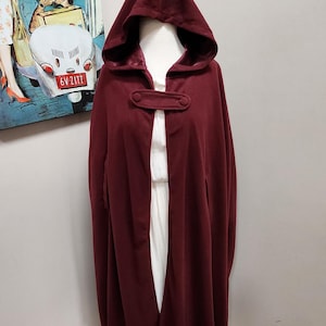 May include: A burgundy hooded cape with a single button closure. The cape is made of a soft, warm fabric and has a long, flowing design.