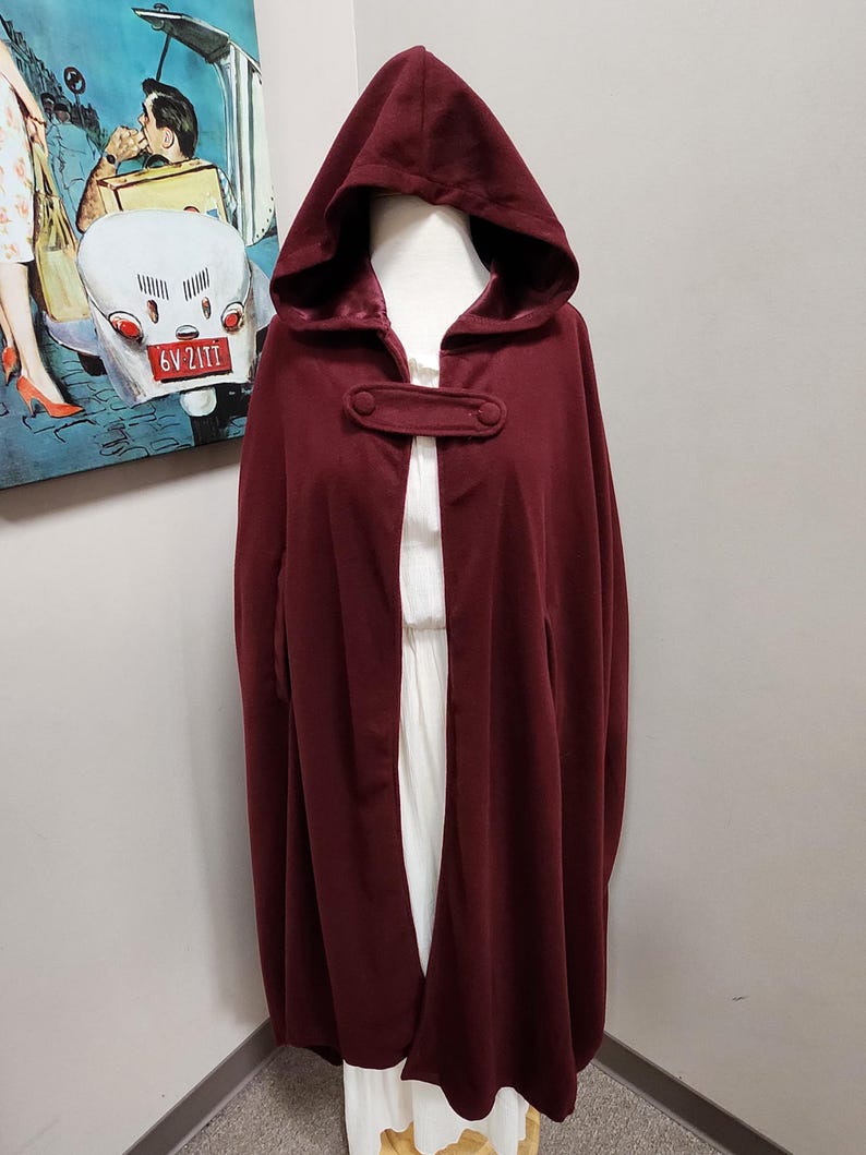 May include: A burgundy hooded cape with a single button closure. The cape is made of a soft, warm fabric and has a long, flowing design.
