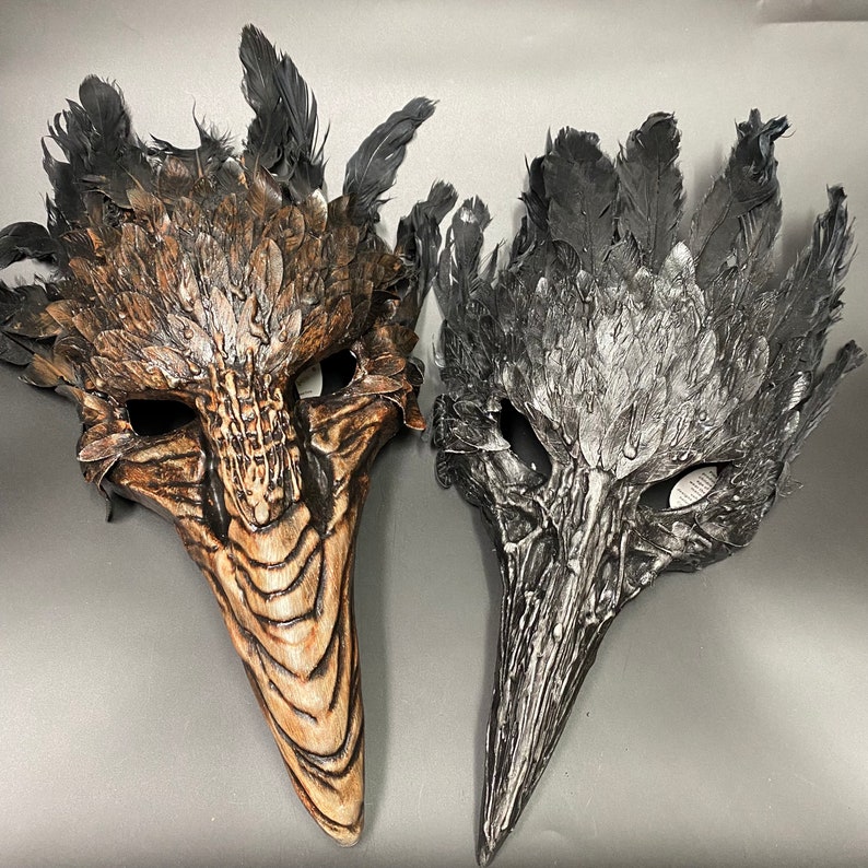 Puede incluir: Dos m&aacute;scaras de carnaval con tem&aacute;tica de p&aacute;jaro. Una m&aacute;scara es marr&oacute;n con plumas negras y la otra es negra con plumas plateadas.