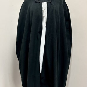 May include: A black hooded cape with a button closure at the neck. The cape is made of a soft, flowing fabric and has a simple, elegant design.