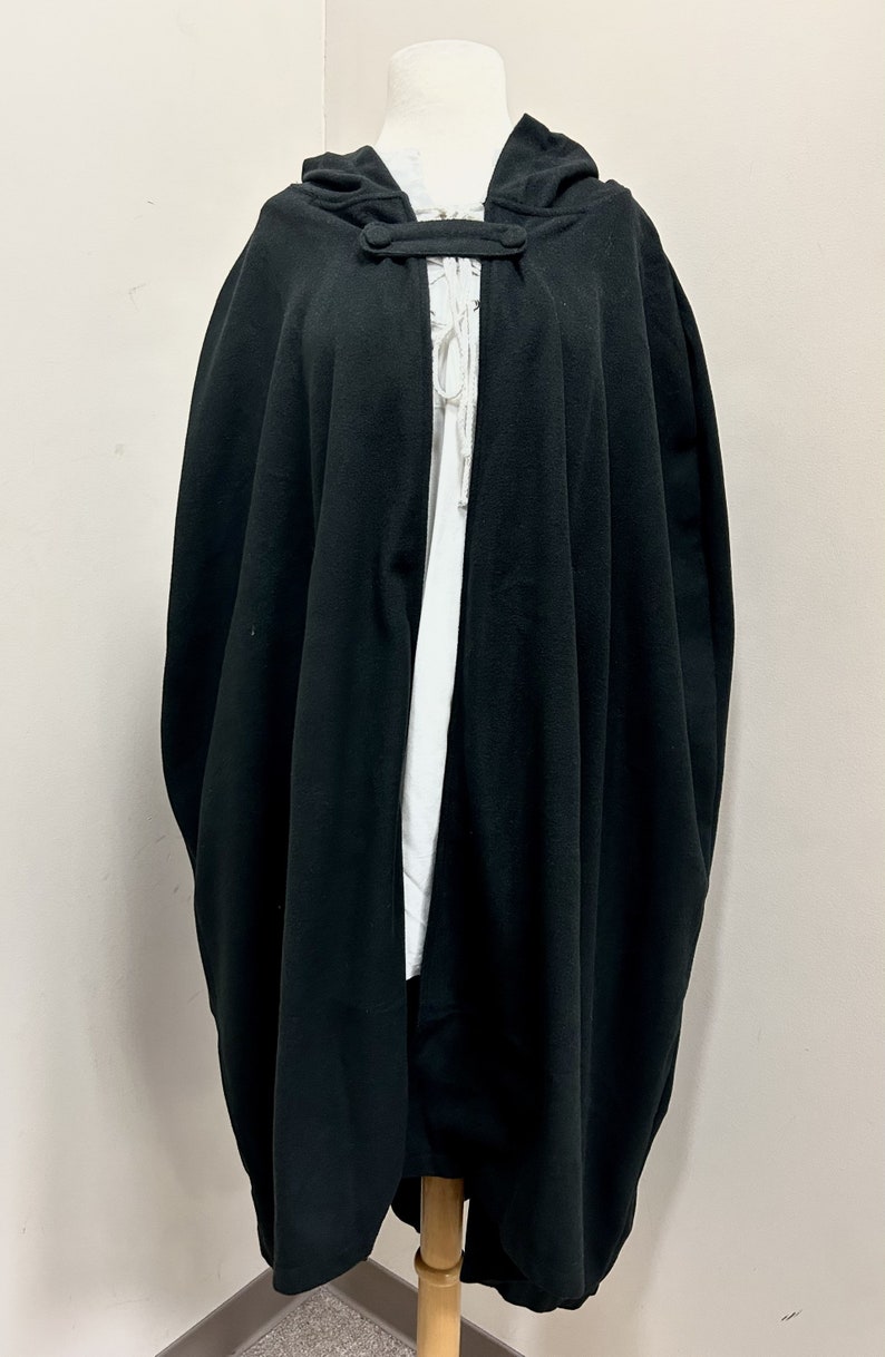 May include: A black hooded cape with a button closure at the neck. The cape is made of a soft, flowing fabric and has a simple, elegant design.