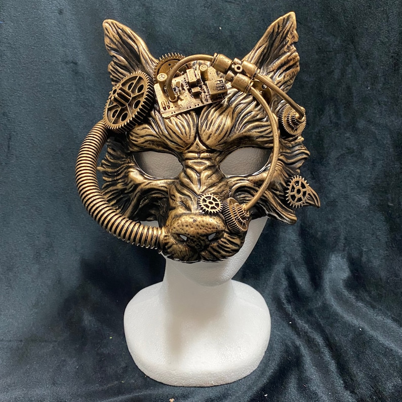 May include: A gold and black wolf mask with steampunk details, including gears and pipes. The mask is on a white mannequin head.