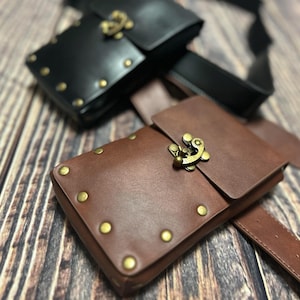 May include: Two leather pouches with metal clasps and rivets. The pouches are brown and black and are attached to a brown leather belt.
