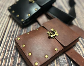 Puede incluir: Dos bolsas de cuero con cierres y remaches de metal. Las bolsas son marrones y negras y están unidas a un cinturón de cuero marrón.