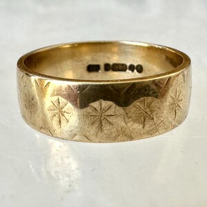 May include: A gold-colored ring with a wide band. The ring's surface is textured with a repeating starburst pattern. The ring has a hallmark stamp on the inside. A piece of jewelry.