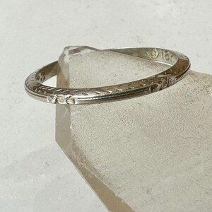 May include: A silver ring with an engraved pattern. The ring is circular and appears to be made of metal. The ring is resting on a clear, geometric surface.