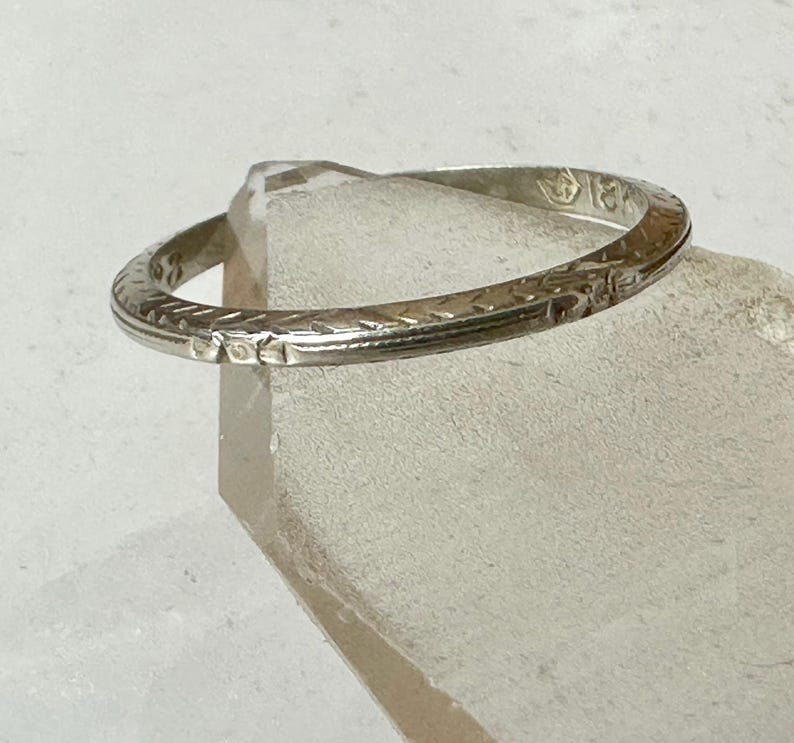 May include: A silver ring with an engraved pattern. The ring is circular and appears to be made of metal. The ring is resting on a clear, geometric surface.