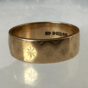 May include: A gold-colored ring with a wide band. The ring's surface is textured with etched starburst patterns. The interior of the ring has markings. A piece of jewelry.