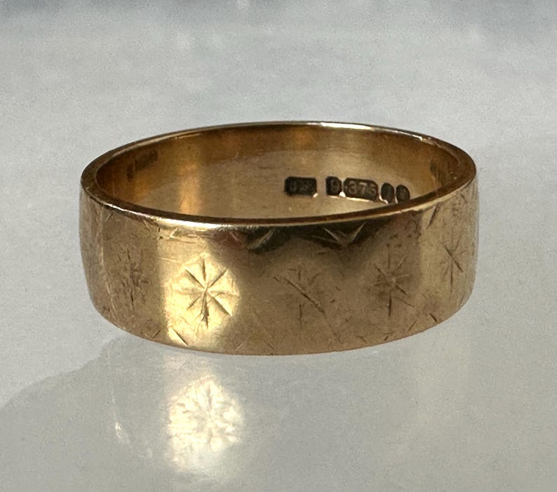 May include: A gold-colored ring with a wide band. The ring's surface is textured with etched starburst patterns. The interior of the ring has markings. A piece of jewelry.
