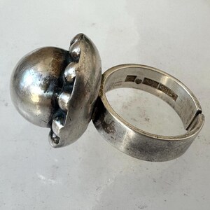May include: A silver ring with a large, spherical design. The ring features a textured, orb-like centerpiece with smaller, rounded accents. The band is thick and has a worn appearance, suggesting an antique or vintage style.