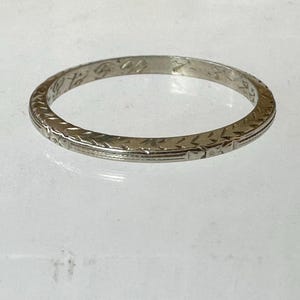 May include: A silver-colored ring with an engraved pattern. The ring has a repeating geometric design around the band. The ring is circular and appears to be made of metal.
