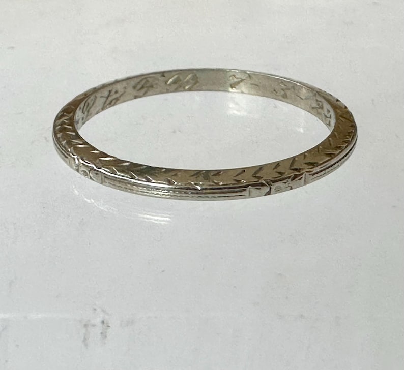May include: A silver-colored ring with an engraved pattern. The ring has a repeating geometric design around the band. The ring is circular and appears to be made of metal.